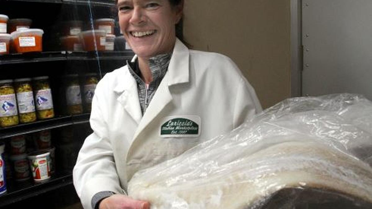 Employee Tracy Holden holds baccala at Lariccia’s Italian Marketplace, where business is “booming,” especially when Italians prepare for the Feast of the Seven Fishes, a Christmas Eve tradition. (Photo by William D. Lewis)