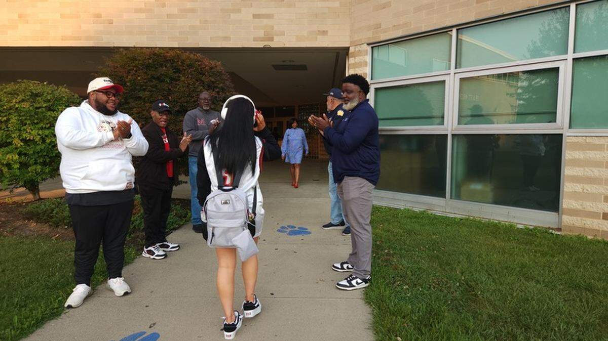 High school student walking into East High School on first day of school in 2024, greeted by Pastor Ernest Ellis, Dr. David Davis, Chip Banks, MLB player Kenneth E. Smith, Mayor Tito Brown and Superintendent Jeremy Batchelor.