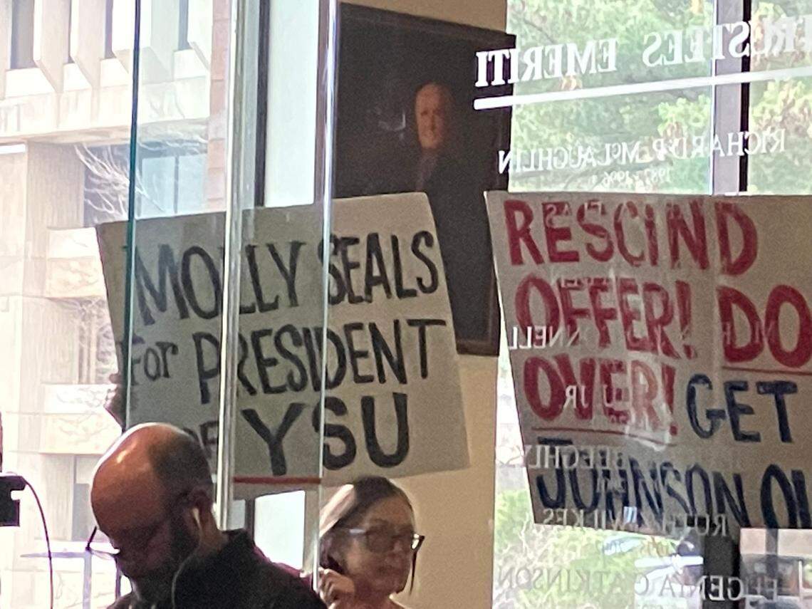 Protesters hold signs during Thursday’s Youngstown State Board of Trustees meeting.
