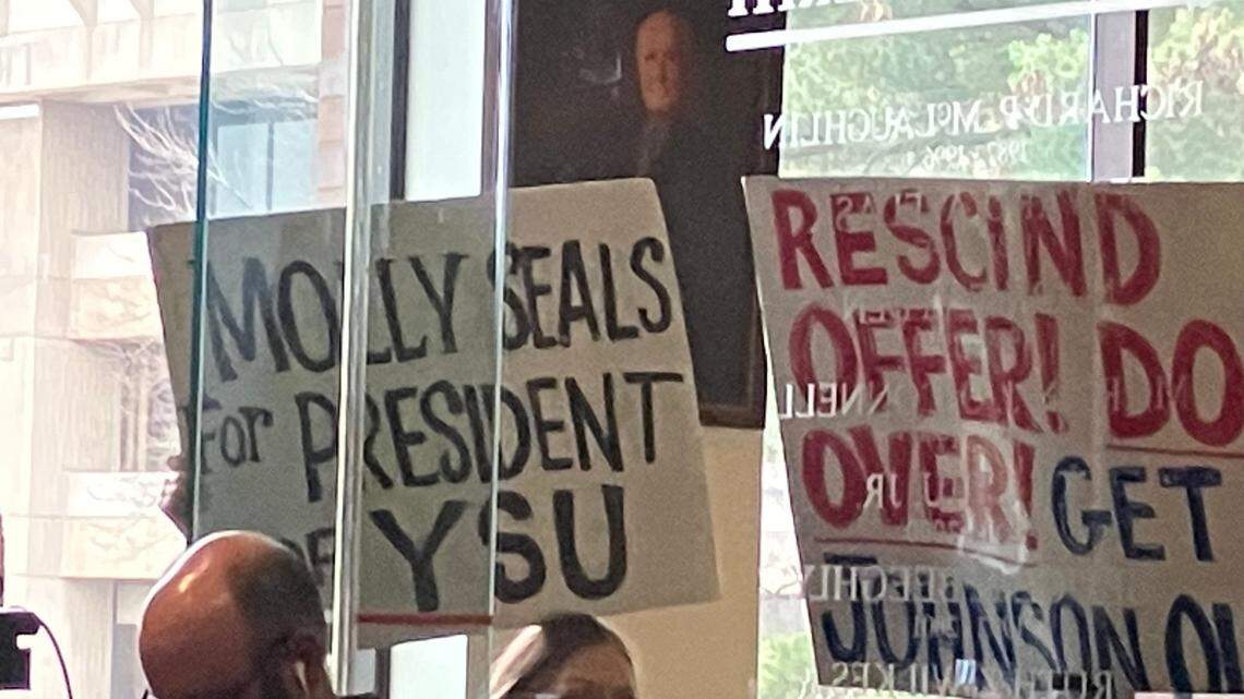 Protesters hold signs during Thursday’s Youngstown State Board of Trustees meeting.
