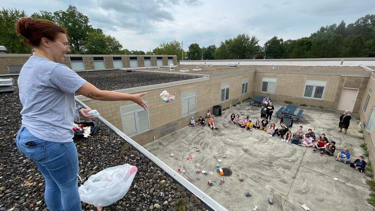 Sebring Local elementary teacher, Alexis Zehnder, puts 4th grade science students’ hand-crafted egg-container devices to the test by dropping them from the rooftop of the elementary school, as they watch from below, in preparation for an upcoming Egg Drop Challenge.