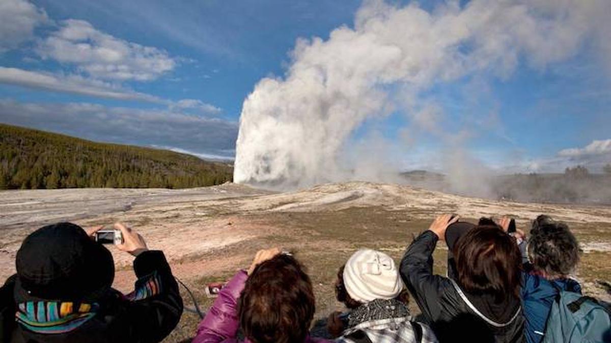 Tourists take photos of Yellowstone Park's most famous geyser. In July 2020, a man ran across Old Faithful multiple times to wave an American flag. He was recently apprehended in Maine, will spend 15 days in prison and is banned from the park. 