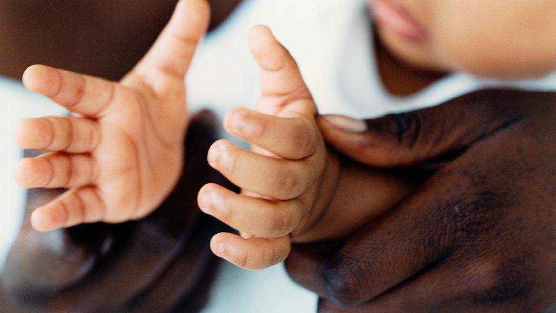 A Black parent holds an infant's hands.