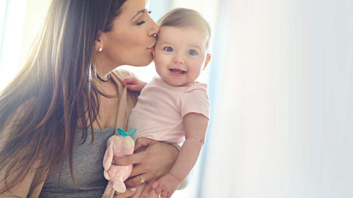Mother, bonding and forehead kiss for baby girl on in house living room, nursery or family home bedroom in trust or love. Smile, happy and infant child with mom in support, security or safety comfort.