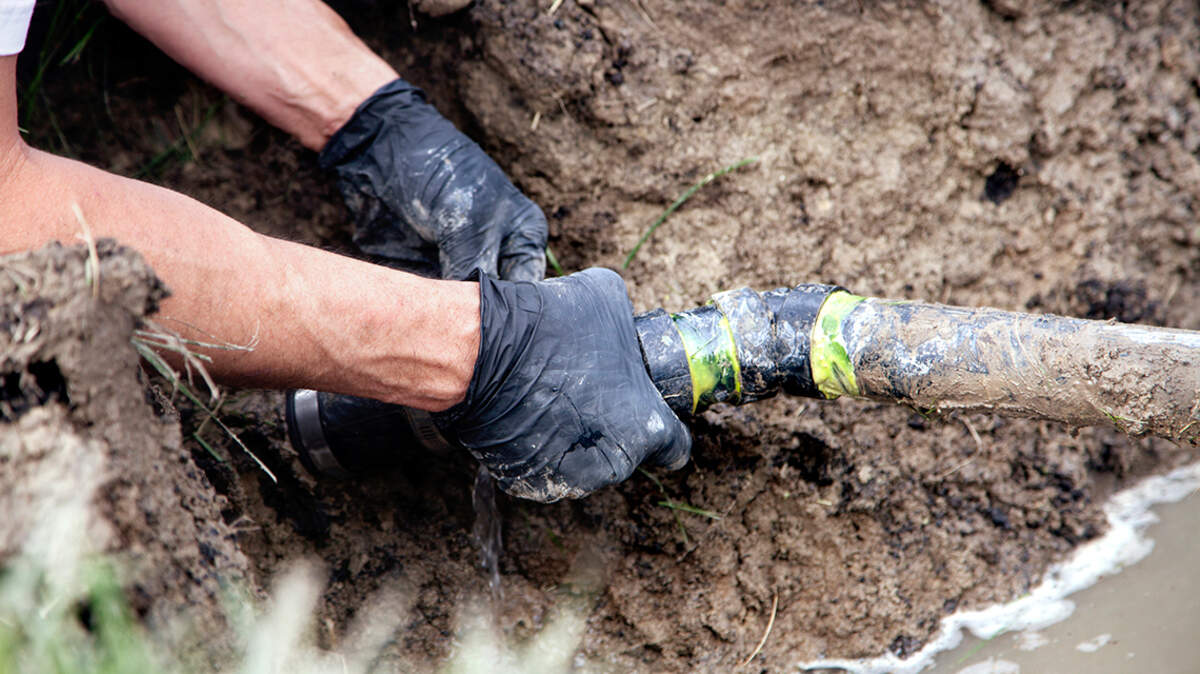 A worker repairs a broken pipe in a septic system.