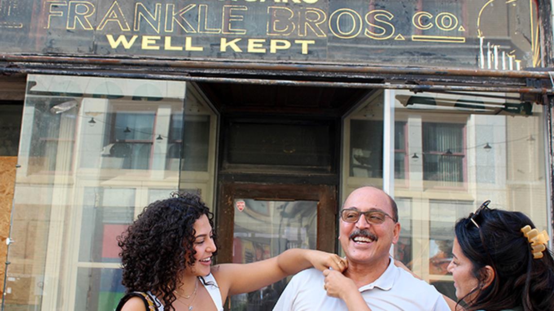 Amer 'Al' Adi Othman grins as his wife, Fidaa (right) and daughter Lana (left) hang a microphone over his shoulder before a TV news interview on Saturday, Sept. 18, 2021. Behind them is the former Pig Iron Press building along North Phelps Street in downtown Youngstown, which Adi's family owns and intends to repurpose.