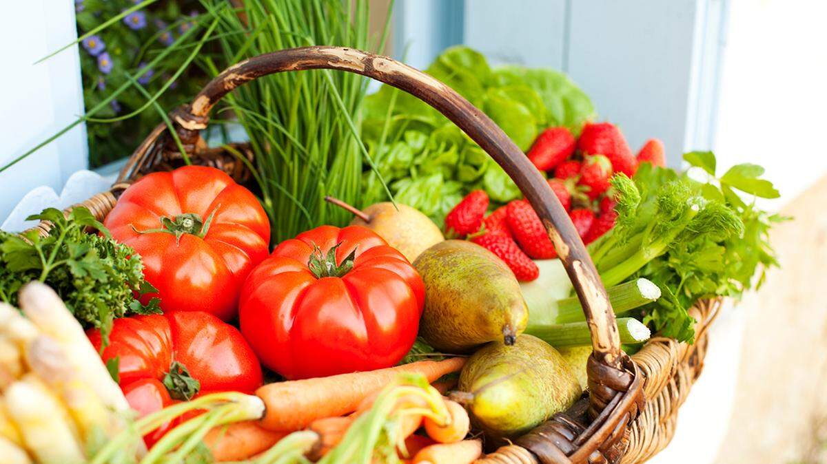 A basket full of strawberries, pears, tomatoes and some lettuce sitting on a windowsill.