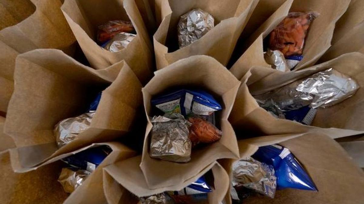 Bagged lunches await stapling before being distributed to students. The Biden administration on Monday announced efforts to provide funding for food for more than 30 million children over the summer. (Rogelio V. Solis | AP)