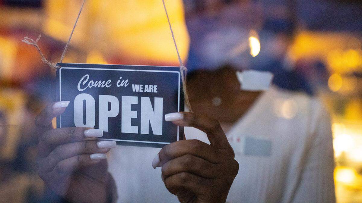 Woman turning an open sign on glass front door of coffee shop. Business owner hanging an open sign at a cafe.